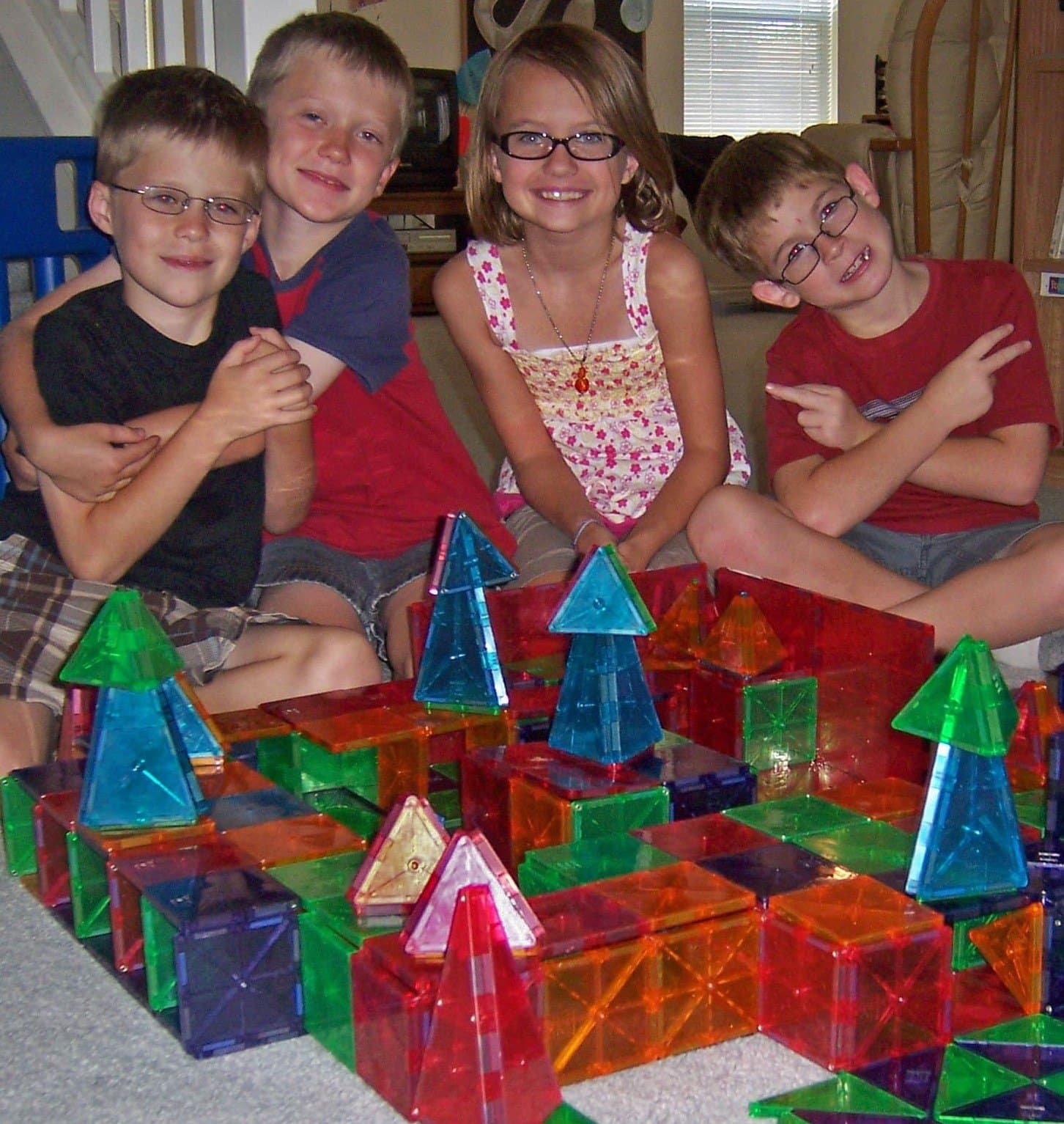 Four Crystal Challenges students sitting behind the castle they built together out of colorful magnetic tiles.